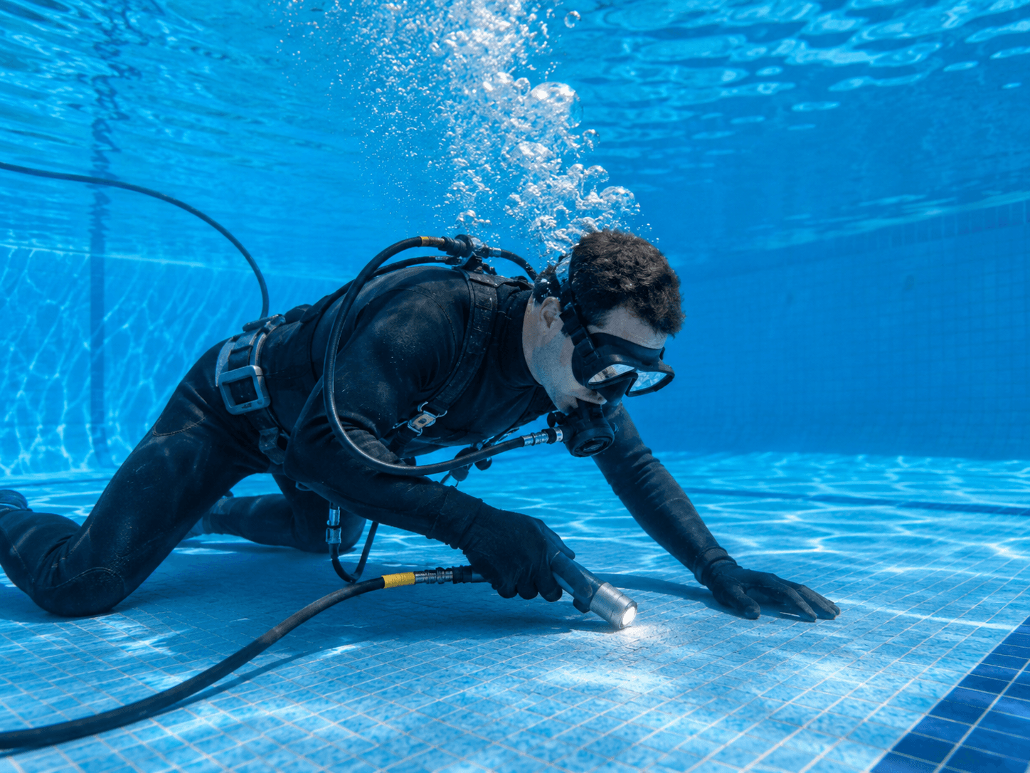 Buzo técnico inspeccionando el vaso de una piscina llena para localizar fisuras y fugas sin vaciar